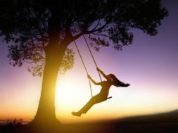 Silhouette Of Happy Young Woman On A Swing With Sunset Backgroun