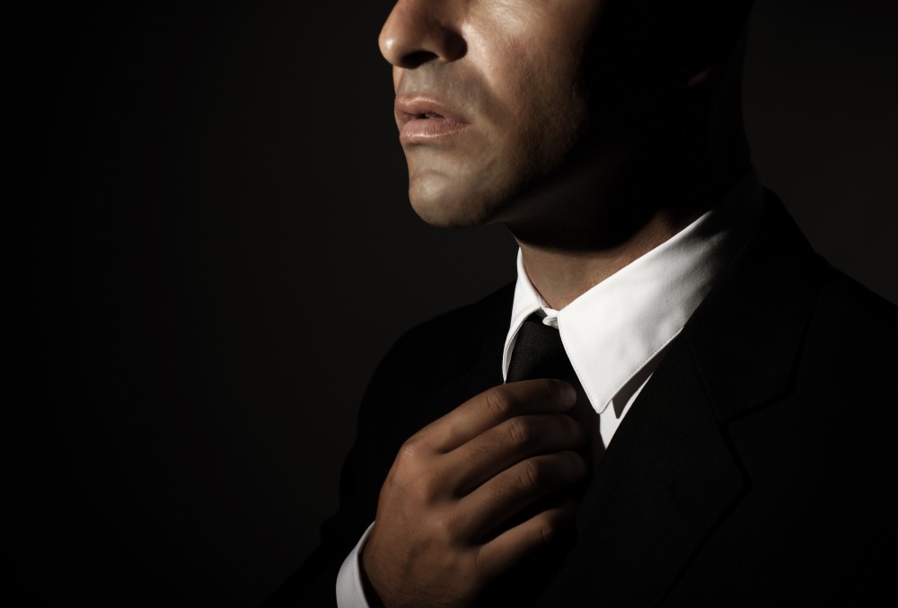 Young handsome man fixed tie isolated on black background, face