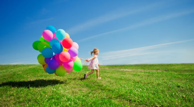 Happy little girl holding colorful balloons. Child playing on a