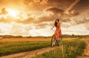 Beautiful woman with old bike in a wheat field